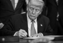 A man in a suit signing a document with a focused expression