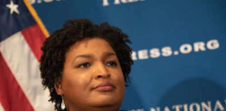 Person speaking at a press conference with flag