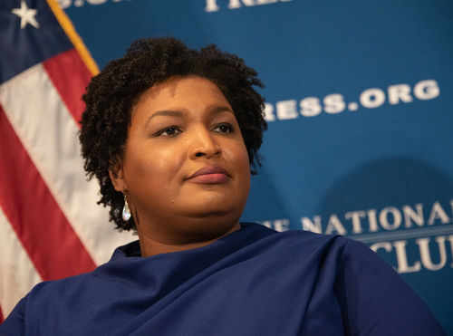 Person speaking at a press conference with flag