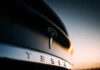 Musk’s Self-Driving Dream COLLAPSES in Courtroom Closeup of Tesla car logo at sunset