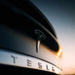 Musk’s Self-Driving Dream COLLAPSES in Courtroom Closeup of Tesla car logo at sunset
