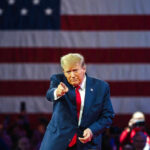 Freedom 250 Meltdown — Who Flipped The Script? Man points in front of American flag backdrop.