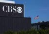 Attack Raises Hate Crime Questions CBS sign on building, American flag in background.