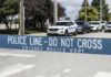 Police line barrier with parked police cars behind.