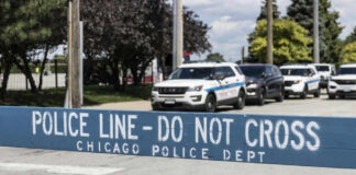 Police line barrier with parked police cars behind.