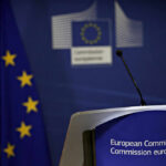 Aid Freeze Threat Over Dutch Kingpin European Commission podium and flag background.