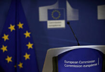 Aid Freeze Threat Over Dutch Kingpin European Commission podium and flag background.