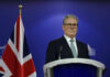 Party Knife-Fight Ousts PM—Who Steps In? Man in suit at a podium, British flag behind.