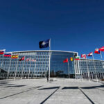 NATO headquarters with member flags in front under a clear blue sky