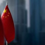 Journalist Tied To China? DOJ Drops Bomb Close-up of the Chinese flag on a flagpole with a blurred urban background