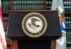 Iran Smuggling Ring Exposed — Sailors at Risk Podium with the Department of Justice seal and American flag in the background