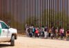 DHS Targets Officials Over Missing Children Group of children and adults walking near a border wall with a customs vehicle