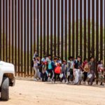 DHS Targets Officials Over Missing Children Group of children and adults walking near a border wall with a customs vehicle