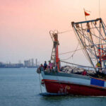 Fishing boat on the water during sunset with an industrial area in the background