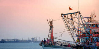 Fishing boat on the water during sunset with an industrial area in the background