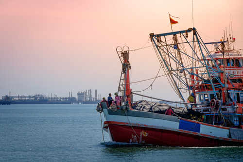 Small,Fishing,Boat Fishing boat on the water during sunset with an industrial area in the background