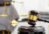 Daycare Scandal Engulfs Ex-Lawmaker A wooden gavel resting on a sound block with a blurred scale of justice in the background