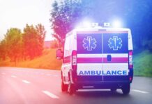 Key Epstein Figure Dies Amid Investigation Ambulance van with flashing lights on a rural road