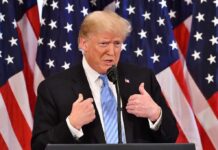 Who Keeps Targeting President Trump? man in suit speaking at podium with US flags behind