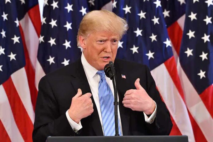 shutterstock_1200585187 man in suit speaking at podium with US flags behind