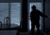 Silhouetted person in a dark room near a door with blinds