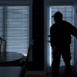 Silhouetted person in a dark room near a door with blinds