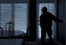 Silhouetted person in a dark room near a door with blinds