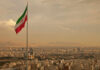 Five-Hour U.S. Blitz Hits Iran Iranian flag waving over a city skyline with mountains in the background