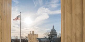 U.S. Capitol seen between marble columns with flag and statue in foreground