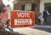Red voting sign with arrow near people entering a polling place