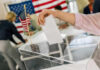 Election Commission Faces Major Shake-Up Hand placing ballot in box with American flag nearby