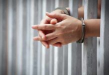 hands in handcuffs behind jail bars