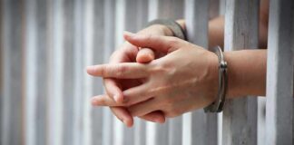 hands in handcuffs behind jail bars