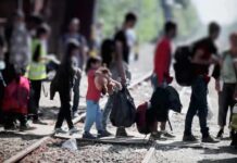 Senate Bill Targets Welfare For Noncitizens People with bags walking along railway tracks