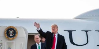 Man in suit waves from aircraft staircase