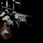 DOJ Lets Bombshell Injunction Hit Close-up of hands holding a rifle in low light