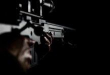 DOJ Lets Bombshell Injunction Hit Close-up of hands holding a rifle in low light
