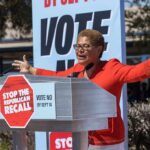 Speaker at outdoor rally behind podium with vote signs