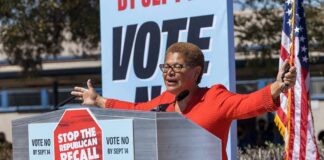 Speaker at outdoor rally behind podium with vote signs
