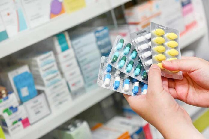 Hands holding blister packs of assorted pills in a pharmacy