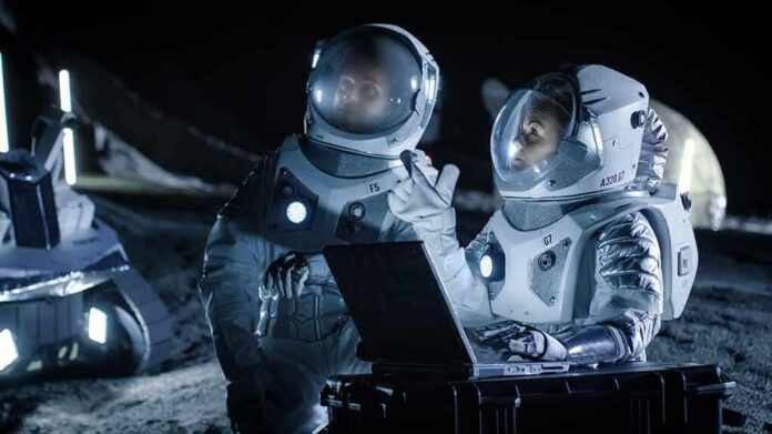 shutterstock_1042736263 Two astronauts in spacesuits review data on a laptop on a moonlike surface at night