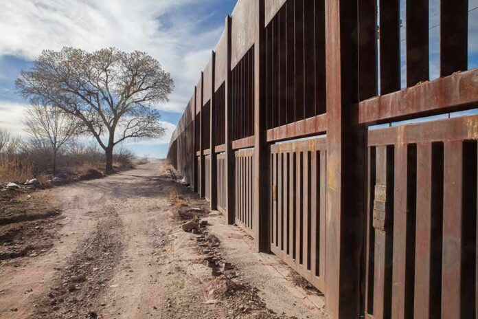 shutterstock_1121257637 Rusty metal border fence along a dirt road with a lone tree