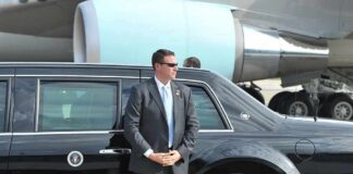security agent in suit standing beside black limousine near aircraft