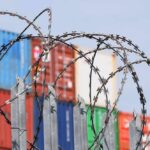 Congress Targets China’s Paper Swap Pipeline Razor wire fence in front of stacked shipping containers