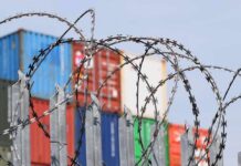 Congress Targets China’s Paper Swap Pipeline Razor wire fence in front of stacked shipping containers