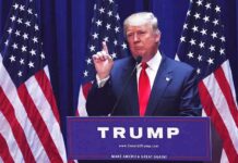 Trump Draws Line On Global Taxes man in suit speaking at podium with multiple American flags