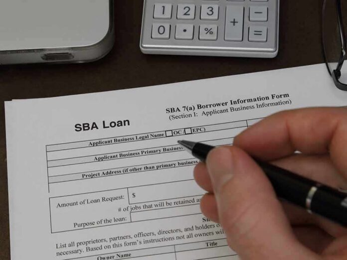 shutterstock_1706130244 Hand holding pen over SBA loan application form