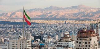 Iranian flag over a dense cityscape with mountains in the background