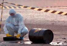 Bomb Squad Swarms U.S. Air Base Hazmat worker kneeling near a fallen barrel at a cordoned-off site