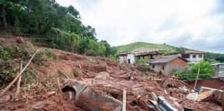 Landslide debris covering houses and a buried car on a muddy hillside